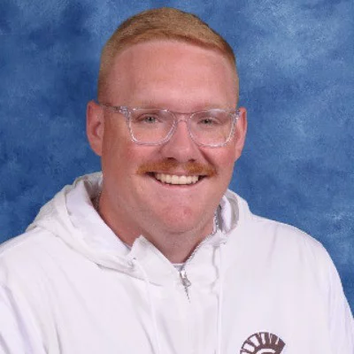 David Olson, a white man with clear glasses, wearing a white zip-up hooded sweatshrit, smiling, against a blue background